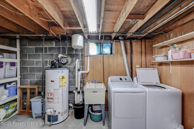 laundry room with laundry area, a sink, wood walls, water heater, and washing machine and dryer