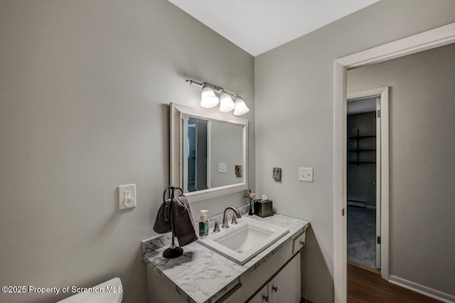 half bathroom with baseboard heating, wood finished floors, vanity, baseboards, and toilet