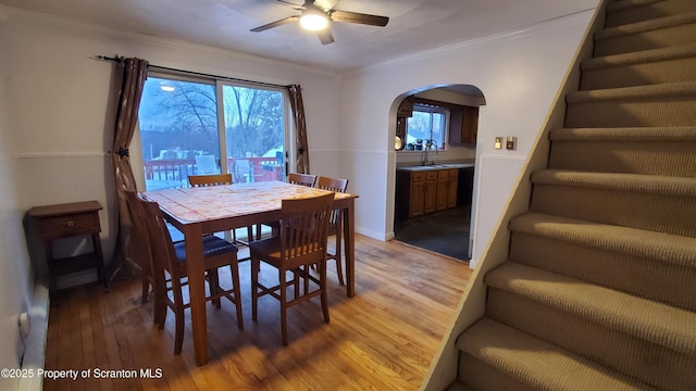 dining space featuring arched walkways, ornamental molding, light wood-type flooring, plenty of natural light, and stairs