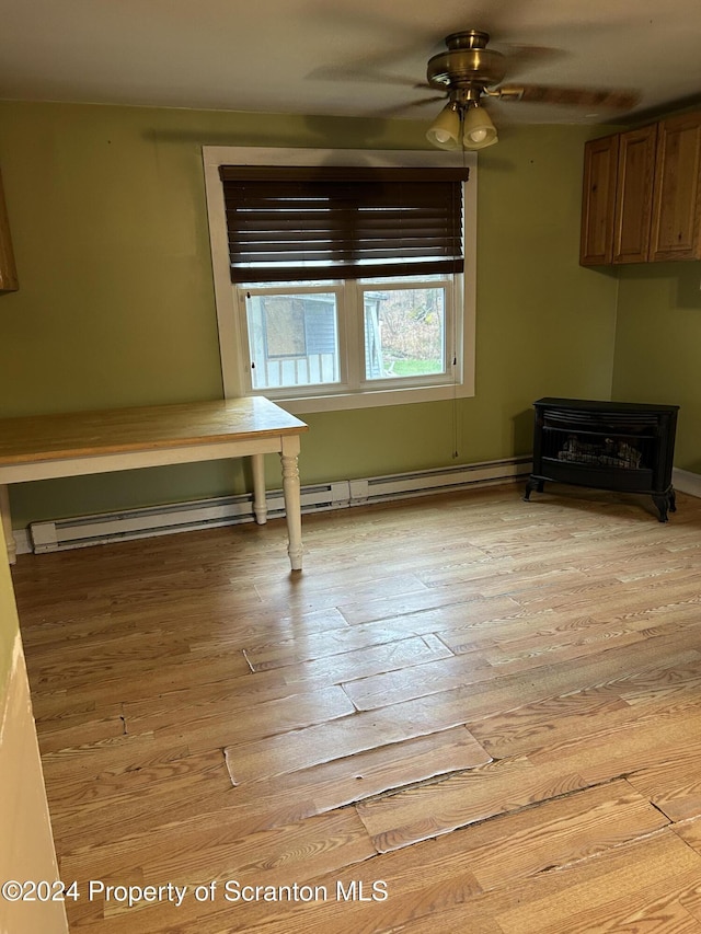 unfurnished dining area featuring a wood stove, baseboard heating, light hardwood / wood-style flooring, and ceiling fan