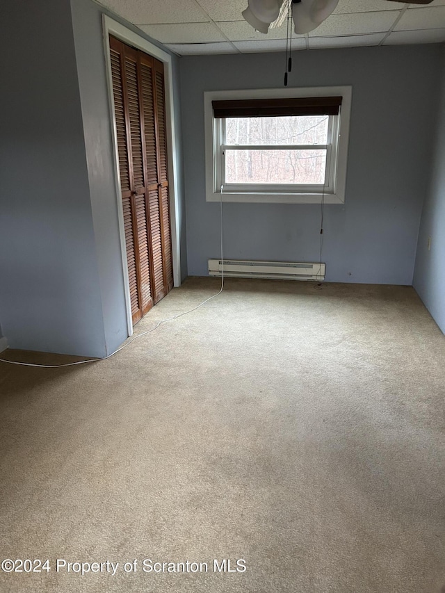 carpeted empty room with a drop ceiling, ceiling fan, and baseboard heating