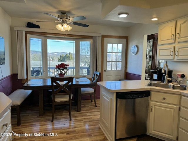 kitchen with light countertops, white cabinetry, light wood-type flooring, dishwasher, and a peninsula