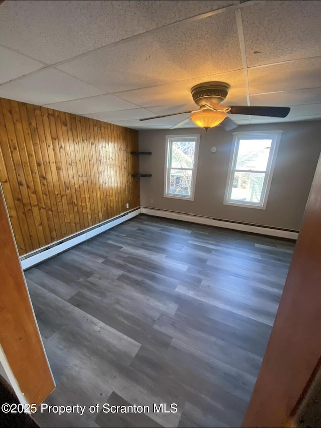 spare room with a drop ceiling, wooden walls, dark hardwood / wood-style floors, and a baseboard radiator