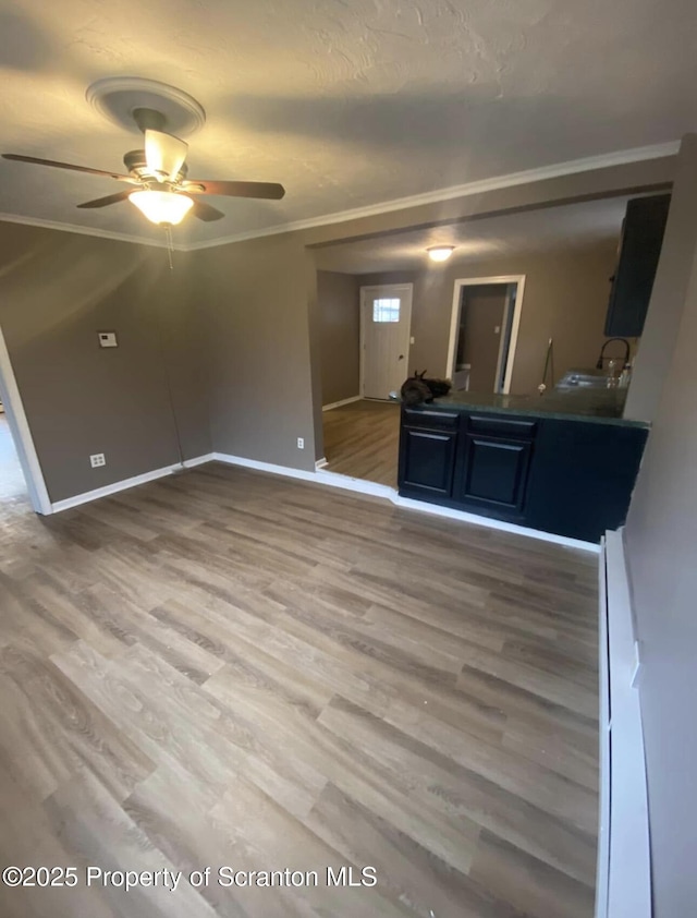 unfurnished living room featuring ceiling fan, ornamental molding, wood-type flooring, and sink