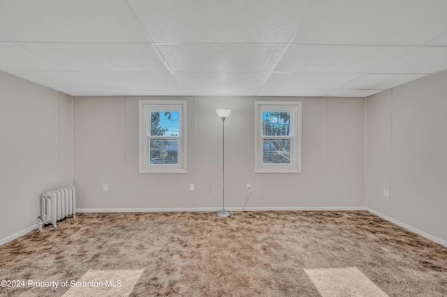 carpeted spare room with radiator, a paneled ceiling, and a wealth of natural light