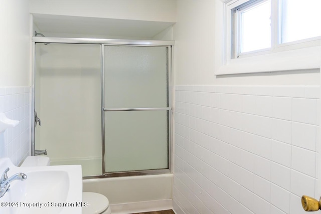 full bathroom featuring shower / bath combination with glass door, toilet, tile walls, and sink