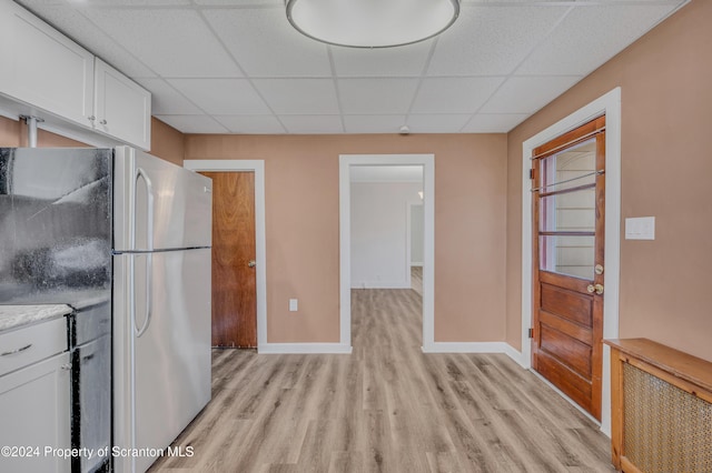 kitchen with a drop ceiling, radiator, stainless steel fridge, light wood-type flooring, and white cabinetry