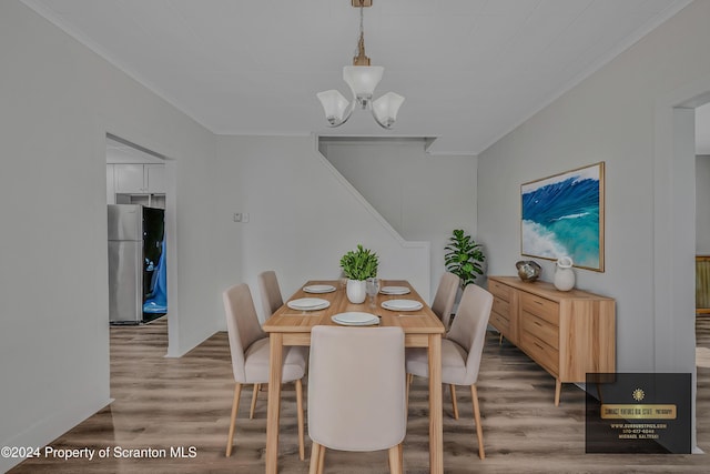 dining room with wood-type flooring, crown molding, and an inviting chandelier