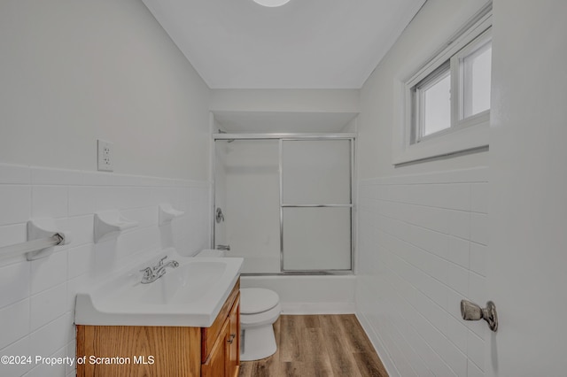 full bathroom featuring combined bath / shower with glass door, hardwood / wood-style flooring, toilet, and tile walls