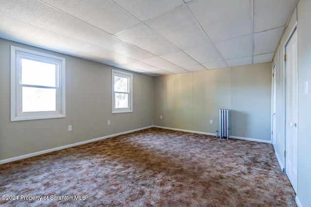 empty room featuring radiator, a drop ceiling, and carpet floors