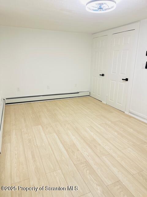 unfurnished room featuring a baseboard radiator and light wood-type flooring