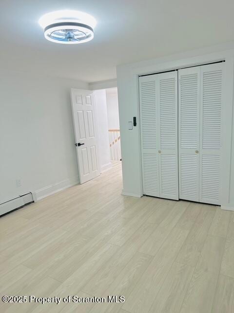 unfurnished bedroom with a baseboard heating unit, a closet, and light wood-type flooring