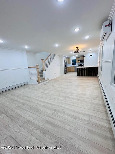 unfurnished living room with a baseboard radiator, crown molding, a wall unit AC, and light hardwood / wood-style floors