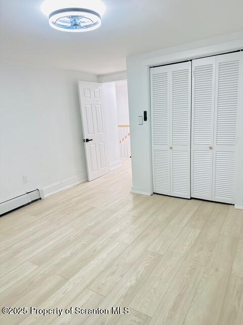 unfurnished bedroom featuring a baseboard radiator, a closet, and light hardwood / wood-style flooring