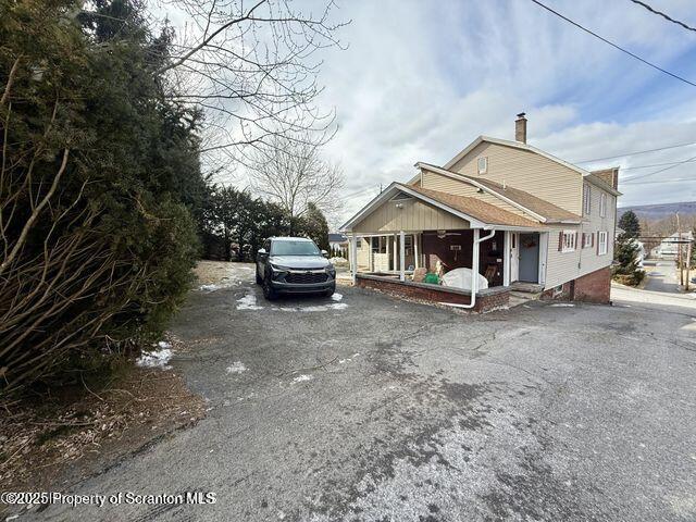 view of front of house with aphalt driveway, a porch, and a chimney