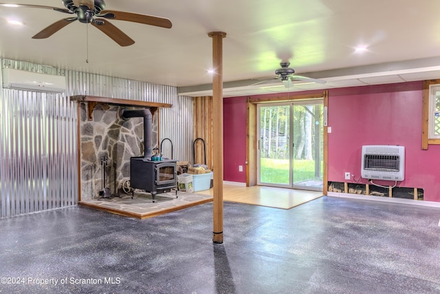 basement featuring a wall mounted air conditioner, heating unit, a wood stove, and ceiling fan