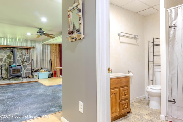 bathroom with toilet, vanity, a wood stove, and ceiling fan