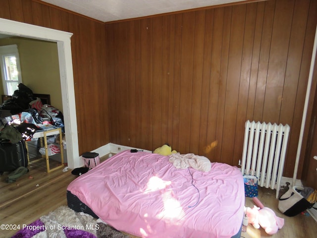 bedroom with radiator heating unit, hardwood / wood-style flooring, and wood walls