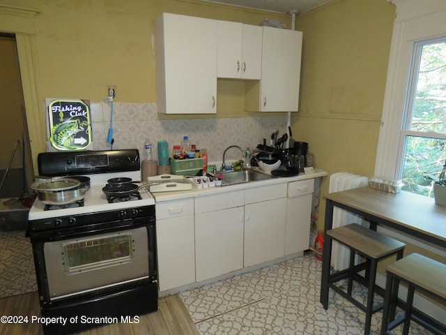 kitchen with white range with gas stovetop, white cabinets, tasteful backsplash, and sink