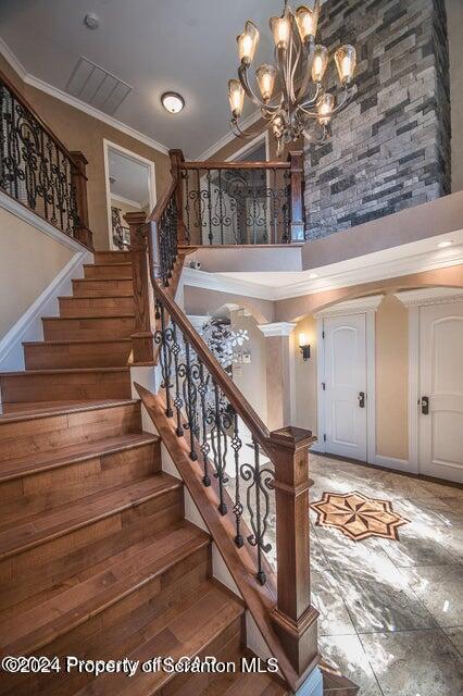 staircase featuring a towering ceiling, a notable chandelier, and ornamental molding