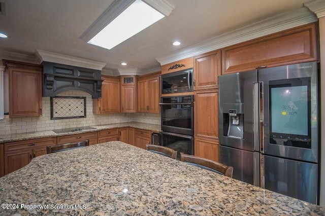 kitchen featuring light stone countertops, backsplash, crown molding, black appliances, and a breakfast bar area