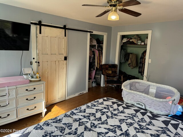 bedroom with a barn door, ceiling fan, and dark wood-type flooring