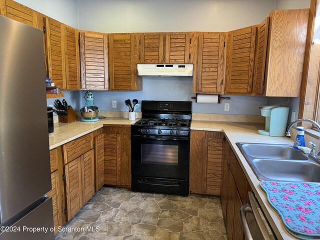 kitchen featuring light countertops, freestanding refrigerator, gas stove, a sink, and under cabinet range hood