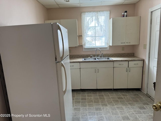 kitchen with freestanding refrigerator, white cabinets, a drop ceiling, and a sink