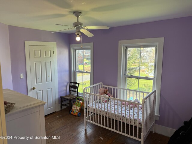 bedroom featuring a crib, dark wood-style flooring, and a ceiling fan