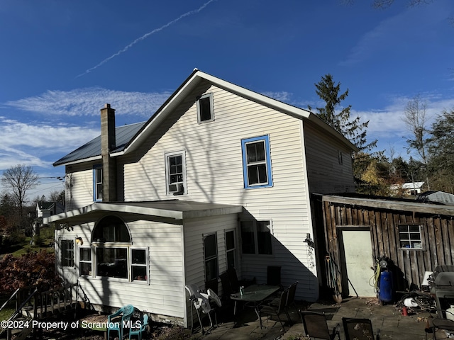 rear view of house featuring a chimney, metal roof, and a patio