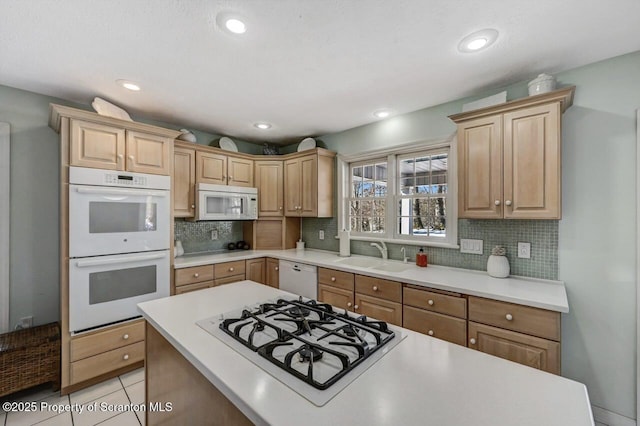 kitchen with light tile patterned floors, light countertops, backsplash, a sink, and white appliances