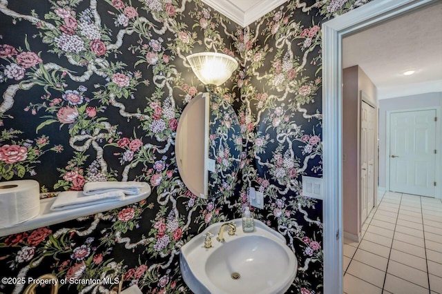 bathroom with wallpapered walls, baseboards, tile patterned floors, crown molding, and a sink