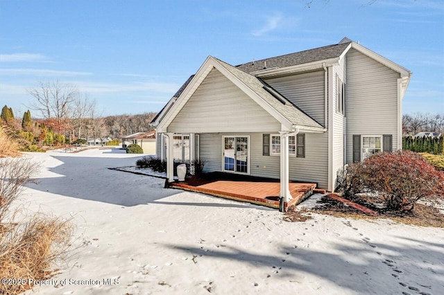 snow covered rear of property with roof with shingles