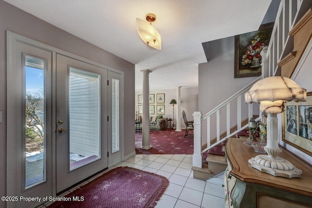 foyer featuring light colored carpet, light tile patterned flooring, ornate columns, and stairs