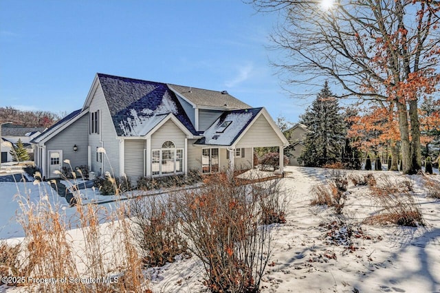 snow covered property with roof with shingles