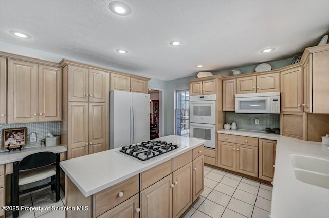 kitchen with light tile patterned floors, light brown cabinets, white appliances, light countertops, and a center island