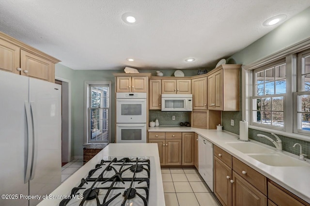 kitchen with light tile patterned flooring, white appliances, a sink, light countertops, and decorative backsplash