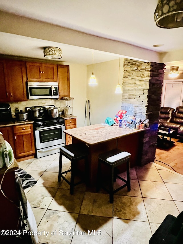 kitchen featuring tasteful backsplash, stainless steel appliances, hanging light fixtures, and light tile patterned flooring