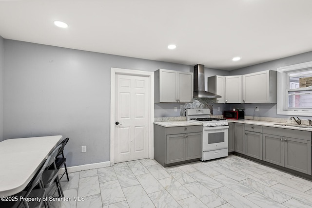 kitchen with marble finish floor, wall chimney range hood, gray cabinets, a sink, and gas range gas stove