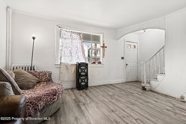 living room featuring crown molding, wood finished floors, stairs, arched walkways, and radiator