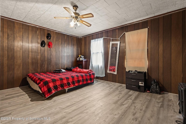 bedroom featuring wooden walls, wood finished floors, and a ceiling fan