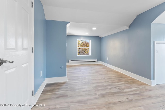 empty room with light wood-type flooring, vaulted ceiling, and a baseboard heating unit