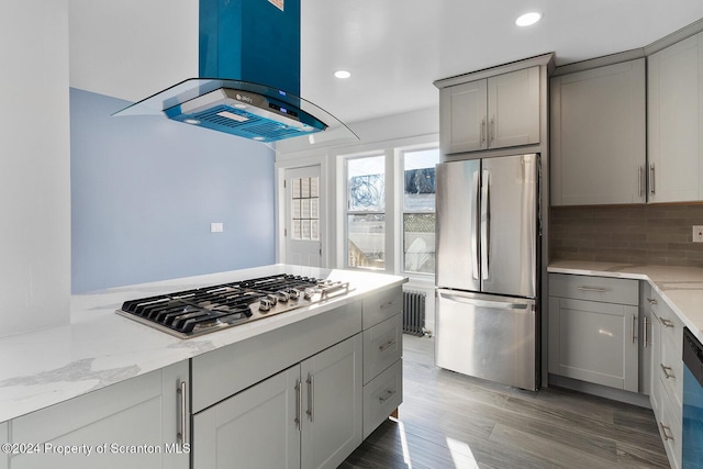 kitchen featuring island exhaust hood, light stone counters, radiator, gray cabinetry, and stainless steel appliances