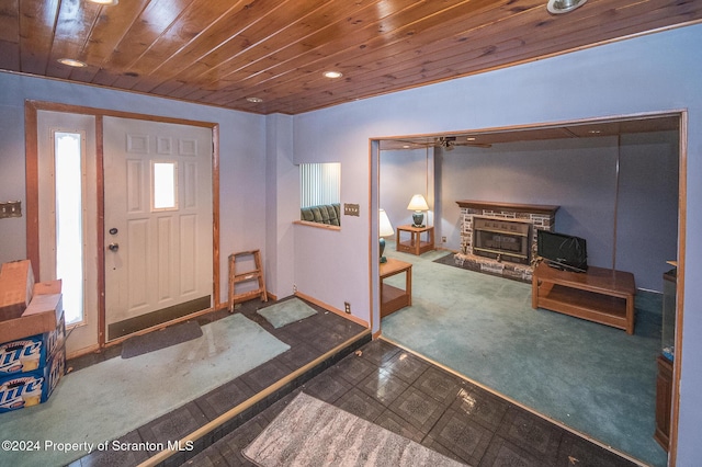 entryway with carpet, a stone fireplace, and wooden ceiling