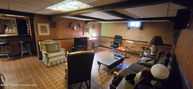 tiled living room featuring beam ceiling, a paneled ceiling, wood walls, and indoor bar