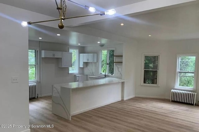 kitchen featuring radiator, kitchen peninsula, white cabinets, and light hardwood / wood-style floors