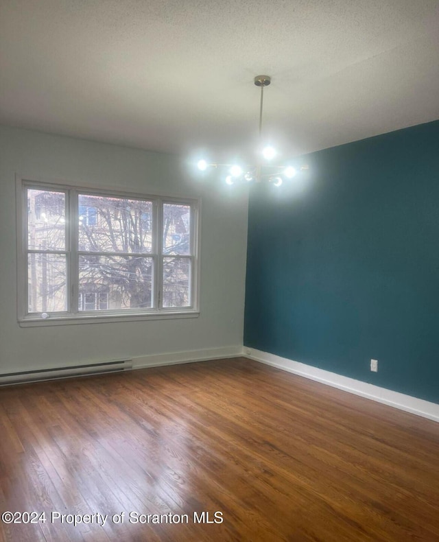 spare room featuring a textured ceiling, hardwood / wood-style flooring, and a baseboard heating unit