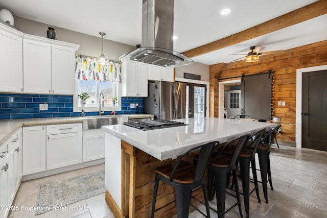 kitchen with a sink, freestanding refrigerator, island range hood, decorative backsplash, and wood walls