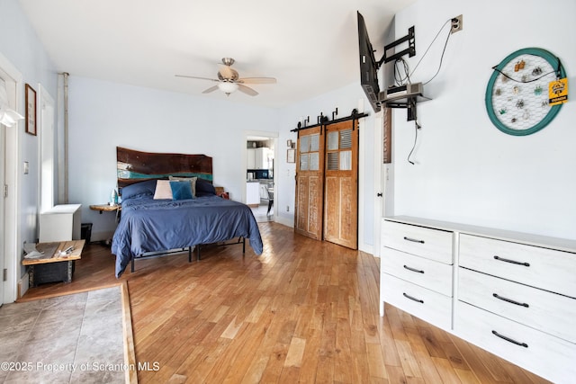 bedroom with a barn door, light wood-style flooring, and a ceiling fan