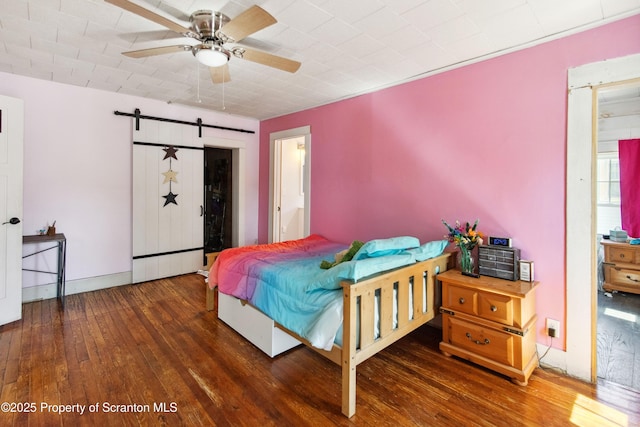 bedroom featuring hardwood / wood-style floors, ceiling fan, and a barn door